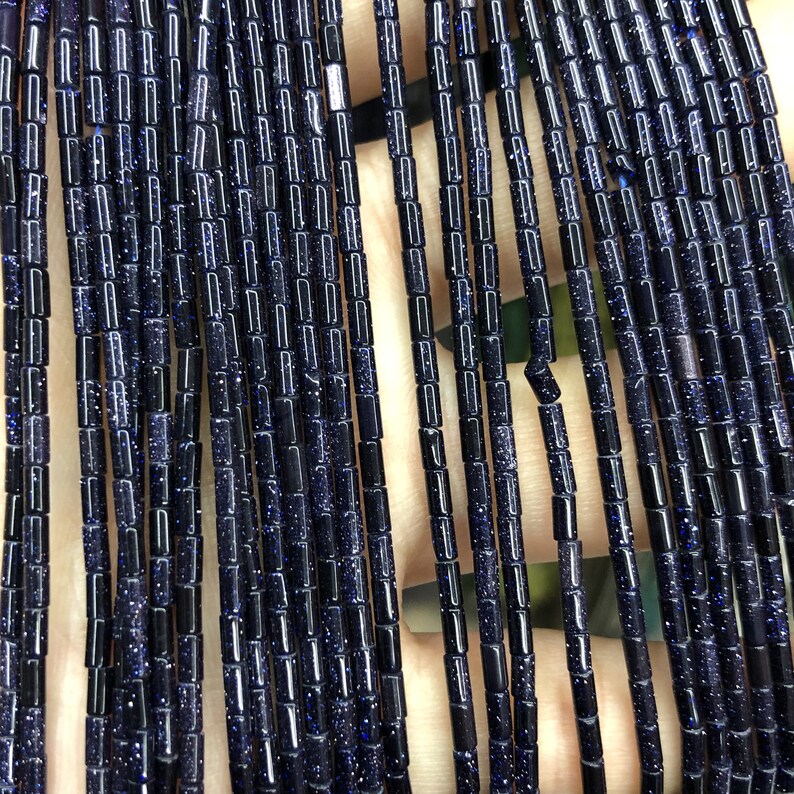 Op de afbeelding: Een streng donkerblauwe edelsteen kralen, elke kraal is een kleine cilinder met een gespikkelde textuur.