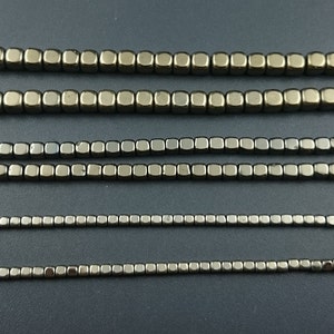 Può includere: Cinque file di perline metalliche quadrate in varie tonalità di grigio e marrone. Le perline sono disposte in linea retta e sono equidistanti.