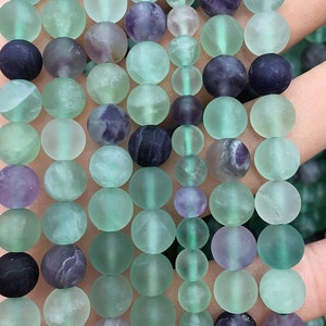 May include: A strand of round, frosted green and purple fluorite beads. The beads are approximately 8mm in diameter and have a smooth, polished finish.