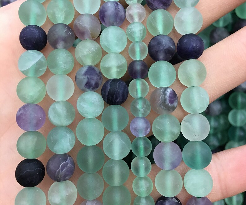 May include: A strand of round, frosted green and purple fluorite beads. The beads are approximately 8mm in diameter and have a smooth, polished finish.