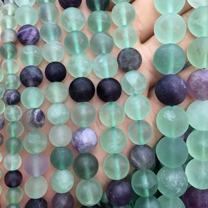 May include: A strand of round, translucent green and purple fluorite beads. The beads are smooth and have a frosted finish.