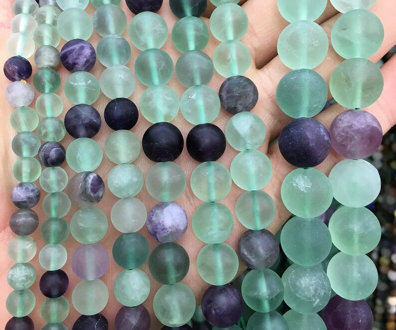 May include: A strand of round, translucent green and purple fluorite beads. The beads are smooth and have a frosted finish.