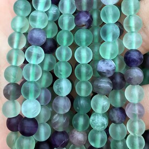 May include: A strand of green and purple fluorite beads. The beads are round and have a frosted finish.