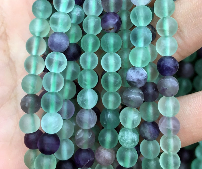 May include: A strand of green and purple fluorite beads. The beads are round and have a frosted finish.
