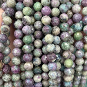 May include: A strand of faceted gemstone beads in shades of green, purple, and grey. The beads are round and have a slightly irregular shape.