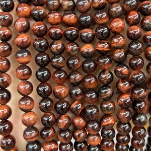 May include: A strand of round, red tiger's eye beads. The beads have a glossy finish and a distinctive chatoyancy, creating a shimmering effect.
