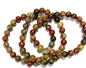 Può includere: Tre braccialetti realizzati con perline di pietra marrone, verde e beige. Le perline sono rotonde e hanno un aspetto naturale e screziato.
