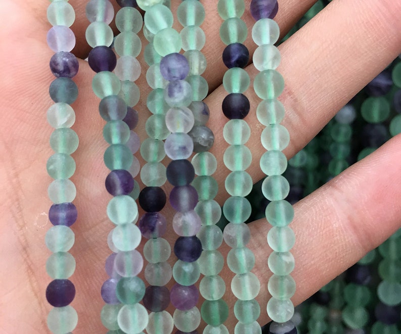 May include: A strand of round, frosted, green and purple fluorite beads. The beads are approximately 6mm in diameter.