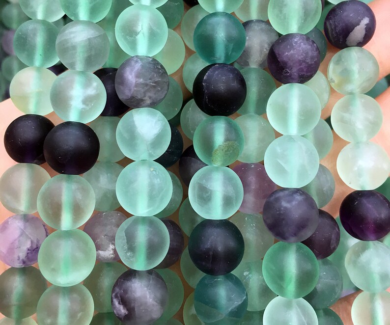 May include: A strand of round, frosted fluorite beads in shades of green, purple, and black. The beads are approximately 8mm in diameter.