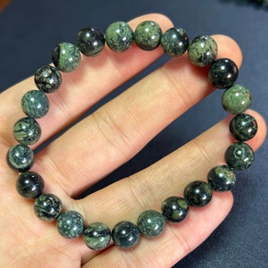Puede incluir: Un brazalete de piedras preciosas verdes y negras con cuentas redondas. Las cuentas tienen un patrón de mármol.