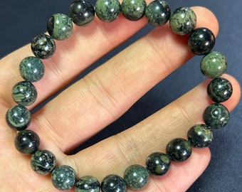 Puede incluir: Un brazalete de piedras preciosas verdes y negras con cuentas redondas. Las cuentas tienen un patrón de mármol.