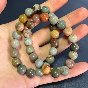 Op de afbeelding: Een armband gemaakt van ronde, gepolijste stenen in verschillende kleuren. De stenen zijn een mix van bruin, beige, grijs en rood.