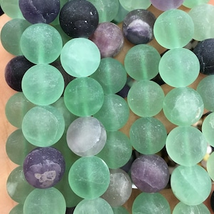 May include: A strand of green, purple, and black fluorite beads. The beads are round and have a frosted finish.