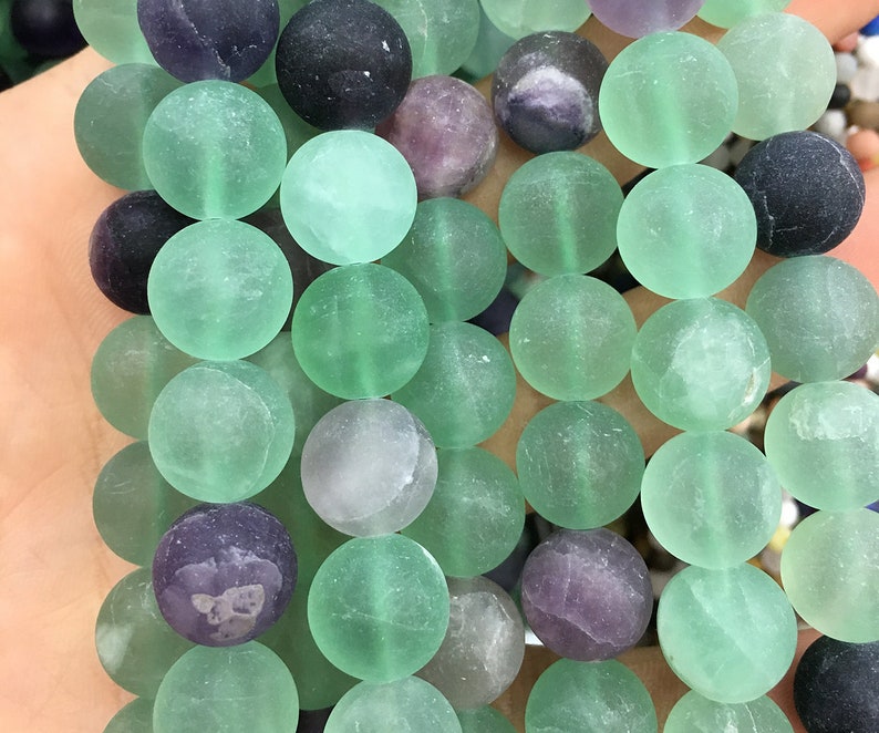 May include: A strand of green, purple, and black fluorite beads. The beads are round and have a frosted finish.