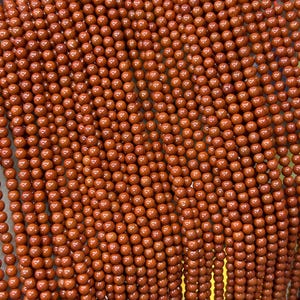 Op de afbeelding: Close-up van strengen ronde, roodbruine kralen. De kralen zijn uniform van grootte en kleur, waardoor een gestructureerd, herhalend patroon ontstaat. De kralen zijn waarschijnlijk voor het maken van sieraden of knutselen.