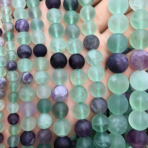 May include: A strand of round, green and purple fluorite beads. The beads are smooth and have a frosted finish.