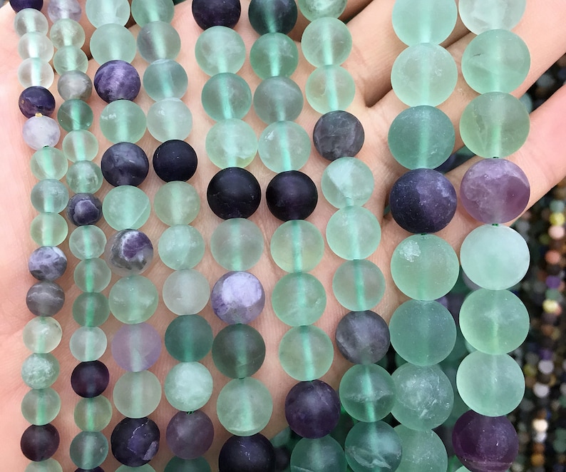May include: A strand of round, green and purple fluorite beads. The beads are smooth and have a frosted finish.