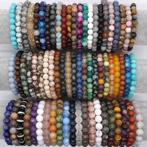 Peut inclure: Une collection de bracelets en pierres précieuses colorées, chacun avec un motif et une couleur différents. Les bracelets sont faits de pierres naturelles et sont disposés en rangées sur un fond blanc.