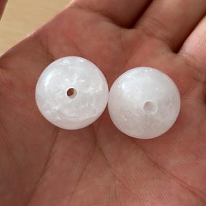 May include: Two round, white, translucent beads with a smooth, polished surface and a central hole. The beads have a crystalline, marbled texture throughout, appearing as small, irregular white fragments embedded within a clear, milky base.