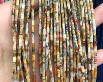 May include: Strands of small, rectangular beads in shades of brown, tan, gray, and white. The beads are strung together, creating a textured and colorful display. The beads appear to be made of a natural stone material.