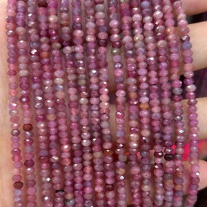 May include: A strand of pink ruby gemstone beads, faceted and round, strung on a thin wire. The beads are approximately 2mm in diameter.