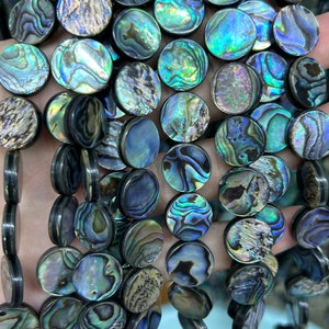 Op de afbeelding: Een streng ronde, iriserende abalone schelp kralen. De kralen hebben een donkerblauwe, groene en paarse kleur met een zwarte rand.
