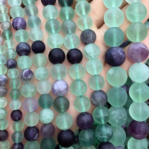 May include: A strand of round, frosted green and purple fluorite beads. The beads are approximately 10mm in diameter and have a smooth, polished finish.