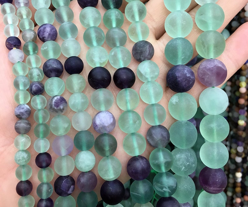 May include: A strand of round, frosted green and purple fluorite beads. The beads are approximately 10mm in diameter and have a smooth, polished finish.