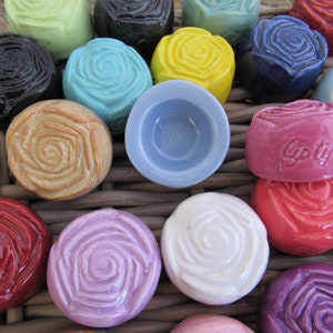 May include: A collection of colorful ceramic rose-shaped items. The items are in various colors, including red, pink, yellow, blue, and black. Some have the word "Giptful" inscribed. The items are arranged in a woven basket.