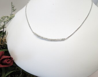 May include: A silver chain necklace with a row of small, white diamonds set in a curved line.