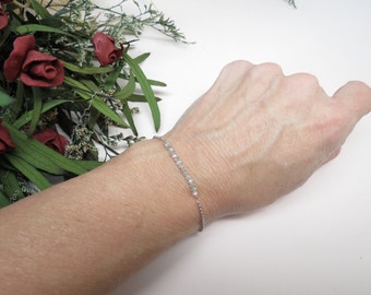 May include: A delicate silver chain bracelet with small, light grey beads.