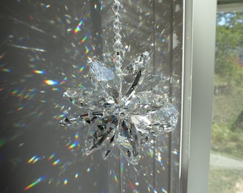May include: A crystal suncatcher with a starburst design hangs from a chain. The suncatcher casts rainbows on the wall behind it.