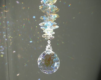 May include: A crystal suncatcher with a large, faceted ball hanging from a chain of smaller, faceted crystals. The suncatcher is casting rainbows on the wall behind it.