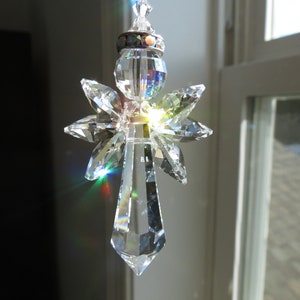 May include: A crystal angel suncatcher with iridescent wings and a clear crystal body. The suncatcher is hanging from a white ceiling.