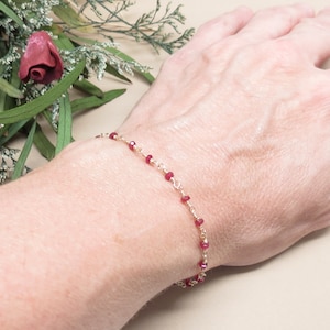 May include: A delicate gold chain bracelet with small red beads.