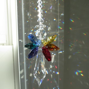 May include: A crystal suncatcher with a clear teardrop-shaped crystal and a rainbow of smaller crystals in the shape of leaves. The suncatcher is hanging from a chain.