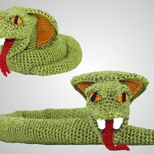 Può includere: Un giocattolo a forma di serpente di colore verde realizzato a uncinetto, con lingua rossa e orecchie arancioni. Il serpente è arrotolato a spirale.