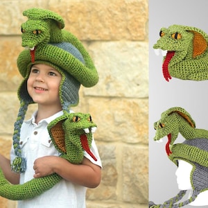 May include: A child wearing a green crocheted snake hat with a long green crocheted snake tail. The hat has a gray crocheted brim and the snake has a red tongue.