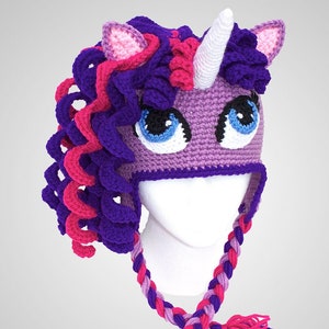 May include: Purple and pink crocheted unicorn hat with a white horn and braided ties.
