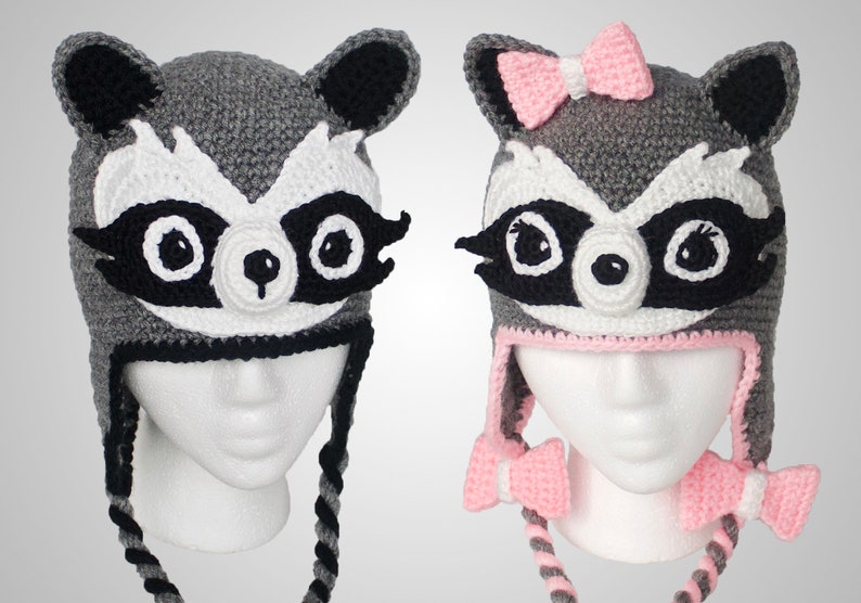 May include: Two gray crocheted raccoon hats with black eyes and white noses. One hat has a pink bow on top.