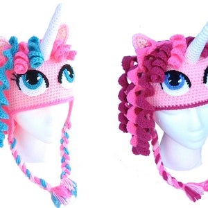 May include: Two pink unicorn hats with crocheted manes and horns. One hat has a blue mane and the other has a pink mane.