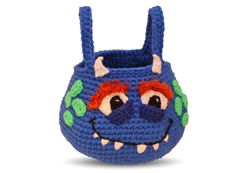 May include: Blue crocheted monster-shaped basket with green spots, orange hair, and white teeth. The basket has two blue handles.