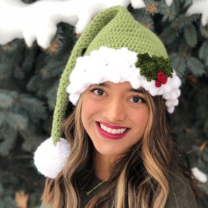 K&ouml;nnte beinhalten: Eine gr&uuml;ne und wei&szlig;e H&auml;kelm&uuml;tze mit einem Weihnachtssterndesign und einem wei&szlig;en Bommel am Ende der M&uuml;tze.