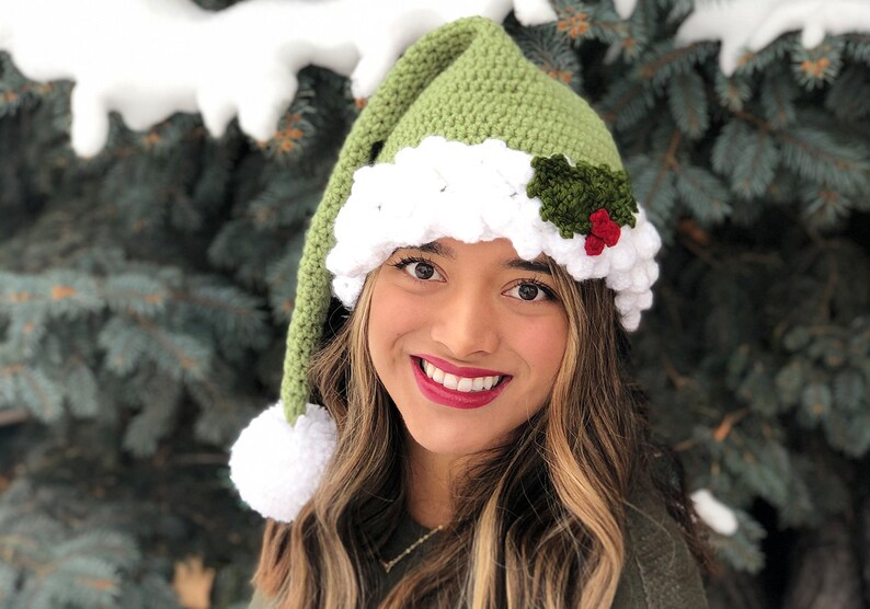 K&ouml;nnte beinhalten: Eine gr&uuml;ne und wei&szlig;e H&auml;kelm&uuml;tze mit einem Weihnachtssterndesign und einem wei&szlig;en Bommel am Ende der M&uuml;tze.