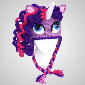 May include: Purple and pink crocheted unicorn hat with a white horn and large blue eyes. The hat has a long braided strap with tassels.