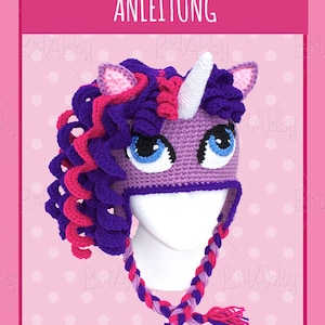 May include: Purple and pink crocheted unicorn hat with a white horn and braided ties. The hat is on a white mannequin head. The background is pink with white polka dots. The text "ANLEITUNG" is at the top of the image.