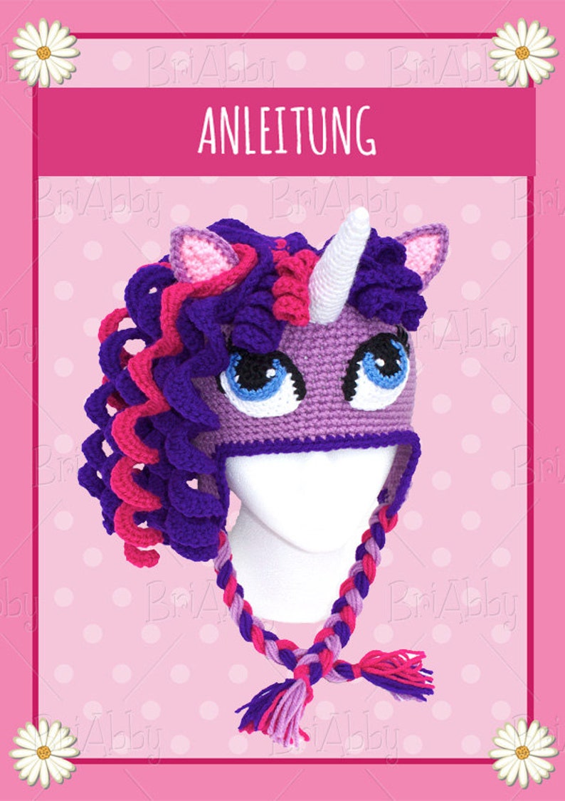 May include: Purple and pink crocheted unicorn hat with a white horn and braided ties. The hat is on a white mannequin head. The background is pink with white polka dots. The text "ANLEITUNG" is at the top of the image.