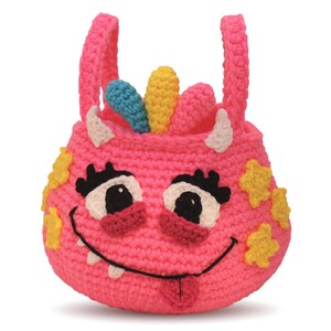 May include: Pink crocheted monster-shaped tote bag with a smiling face, white teeth, a pink tongue sticking out, and yellow stars. The bag has two white horns and a rainbow-colored crest on top.