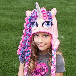 May include: A pink and blue crocheted unicorn hat with a white horn and large blue eyes. The hat has long braids that are pink, blue, and white.