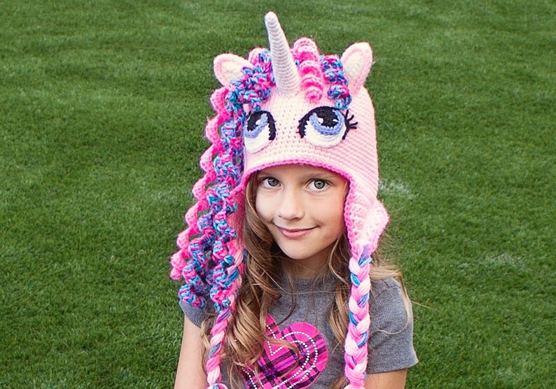 May include: A pink and blue crocheted unicorn hat with a white horn and large blue eyes. The hat has long braids that are pink, blue, and white.